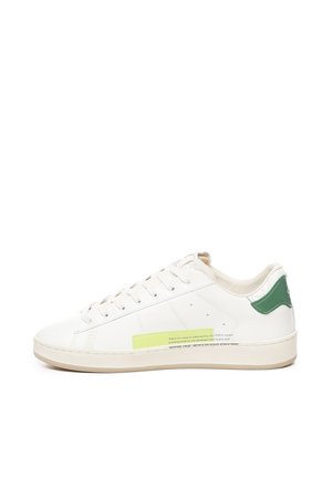 Sneaker bianca in pelle con dettaglio verde sul tallone, suola beige testurizzata e un'etichetta gialla prominente sul lato che presenta un riassunto dell'artigianato.