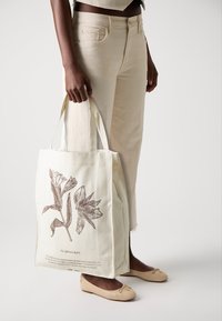Bomullstote i krämvitt med ett brunt botaniskt tryck av liljor. Starka handtag, rektangulär form och slitstark textur.