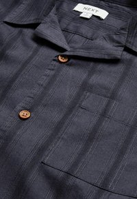 Koszula z krótkim rękawem w ciemnoszarym kolorze, z prążkami, kołnierzykiem, kieszenią na piersi oraz brązowymi guzikami na teksturowanej tkaninie. Metka z napisem "NEXT".