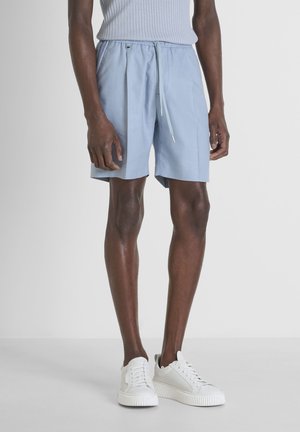 Pantalones cortos azul claro hechos de una tela suave, con una cinturilla elástica ajustable, pliegues al frente y un corte relajado. Los zapatos son blancos con acentos texturizados.