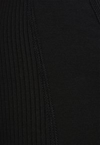 Tissu noir à côtes montrant un gros plan de la texture, avec des coutures lisses contrastantes. La surface semble élastique et moulante.