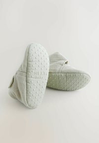 Ljusgrå baby skor med ett mjukt tygövre och texturerade gummisulor med prickar för grepp. En liten etikett syns på sidan.