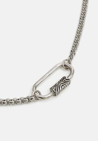 Collier en argent avec un lien central texturé présentant des motifs ondulés, complémenté par de plus petits maillons entrelacés.