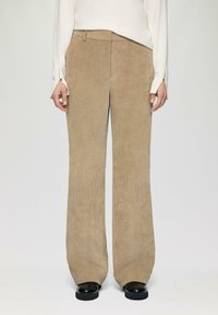 Beige corduroy wijdgevallen broek met verticale ribbels, met een hoge tailleband en subtiele stiksels bij de zakken. Zwarte platformschoenen.