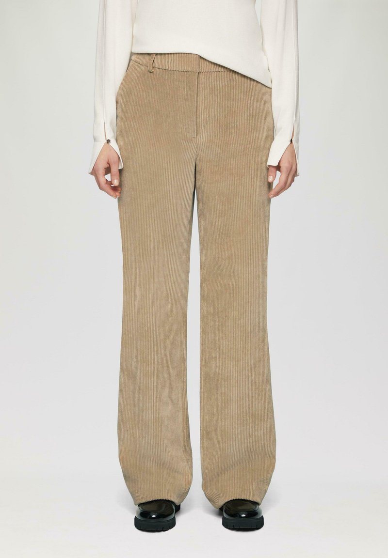 Beige corduroy wijdgevallen broek met verticale ribbels, met een hoge tailleband en subtiele stiksels bij de zakken. Zwarte platformschoenen.
