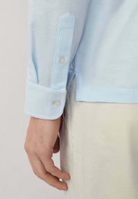 Svijetloplava košulja s dugmadi na manžetama i kontrastnim bijelim dugmadi, koja se odlikuje glatkom teksturom i dizajnom manžeta s nagibom.