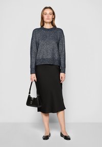 Maglione lavorato a maglia blu navy con collo rotondo e maniche lunghe, abbinato a una gonna nera in satin di lunghezza media e ballerine nere. Piccola borsa nera.