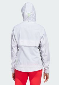 Veste coupe-vent blanche avec capuche, dotée de rayures latérales noires, de détails perforés dans le dos et d'un cordon de serrage au niveau du cou.