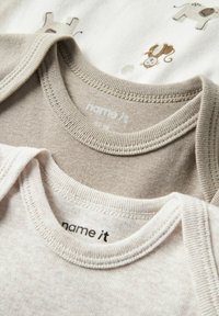 To barneklær stablet oppå hverandre. Den ene har en lys beige farge, den andre en myk krem med dyremønstre. Begge har ribbestrikkede halskanter.