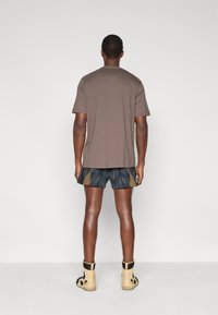 Καφέ βαμβακερό μπλουζάκι, μαύρο σορτς με μοτίβα και χρυσές λεπτομέρειες, και ταμπά μποτάκια με μαύρες λεπτομέρειες. Απλός σχεδιασμός με χαλαρή εφαρμογή.