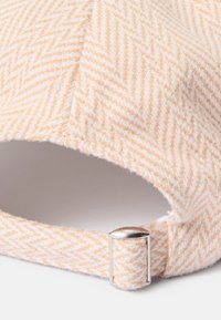 Căciulă peach, cu model herringbone, confecționată dintr-un material moale, având o cataramă metalică argintie la spate și un design fără cusături pentru o ajustare confortabilă.
