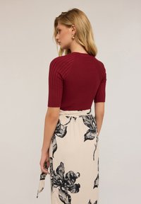 Bordeaux žebrovaný pletený top s krátkými rukávy spárovaný s krémovou sukní se černými květinovými vzory a s páskem kolem pasu.