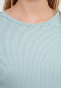 Ανοιχτό γαλάζιο ριμπ μπλουζάκι με στρογγυλή λαιμόκοψη. Το ύφασμα έχει απαλό υφή με διακριτικές κάθετες γραμμές.