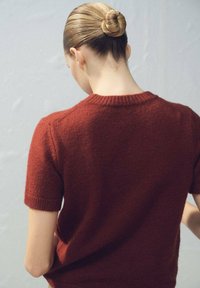 Pull tricoté bordeaux à manches courtes avec encolure ronde et poignets côtelés, doté d'une texture douce et d'une coupe décontractée à l'arrière.
