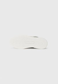 White rubber shoe sole with a textured pattern, featuring a central logo emboss detail and a smooth outer edge for traction.