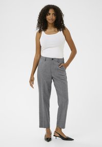 Pantalons ajustés gris clair avec une coupe droite, dotés d'une fermeture à bouton et de poches latérales. Portés avec un débardeur blanc et des talons noirs.