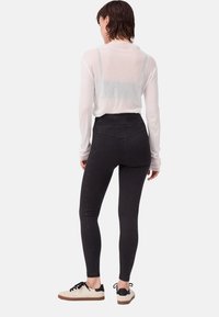 Leggings neri a vita alta realizzati in tessuto elasticizzato, con un design senza cuciture, abbinati a una maglietta bianca a maniche lunghe e scarpe da ginnastica nere e bianche.
