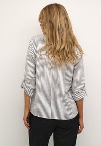 Chemise rayée à coupe décontractée, dotée de manches retroussées et d'un ourlet arrondi. Le tissu a une texture légère, principalement en rayures blanches et bleu marine.
