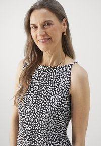 Čierno-biela bezrukávová šaty s texturovanou potlačou, s okrúhlym výstrihom a hladkým materiálom. Zlatý náhrdelník a náušnice ako akcenty.