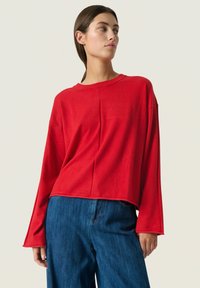 Rød kortærmet top med lange ærmer i blødt stof med en afslappet pasform, parret med mørkeblå brede bukser. Enkel design uden synlige mønstre.