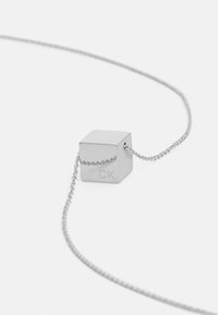 Zilveren kubus hanger aan een eenvoudige ketting, gegraveerd met "CK." Gladde metalen oppervlakte met een gepolijste afwerking, minimalistisch ontwerp.