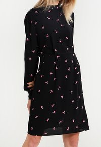 Robe noire à manches longues, taille cintrée et imprimé floral rose éparpillé. Tissu lisse avec une coupe fluide en A.
