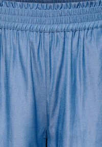 Pantalon bleu clair avec taille élastique, tissu doux froncé et couture centrale visible.