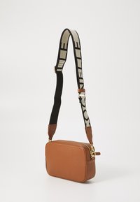 Borsa a tracolla in pelle marrone con texture, zipper dorato e tracolla regolabile in tessuto bianco e nero con design geometrico.