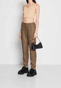 Débardeur court beige avec ourlet à volants, pantalon à carreaux marron, chaussures plates-formes noires épaisses et petit sac à main noir avec bandoulière en chaîne.