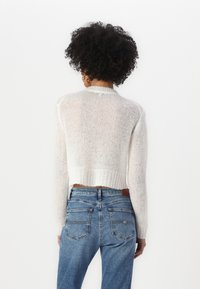 Cropped, lightweight white sweater with a soft texture and ribbed hem; paired with blue high-waisted jeans featuring back pockets.