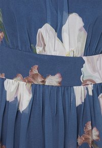 Modrá látková šaty s květinovým vzorem velkých bílých a růžových květin, s nabíraným pasem a hladkým páskem.