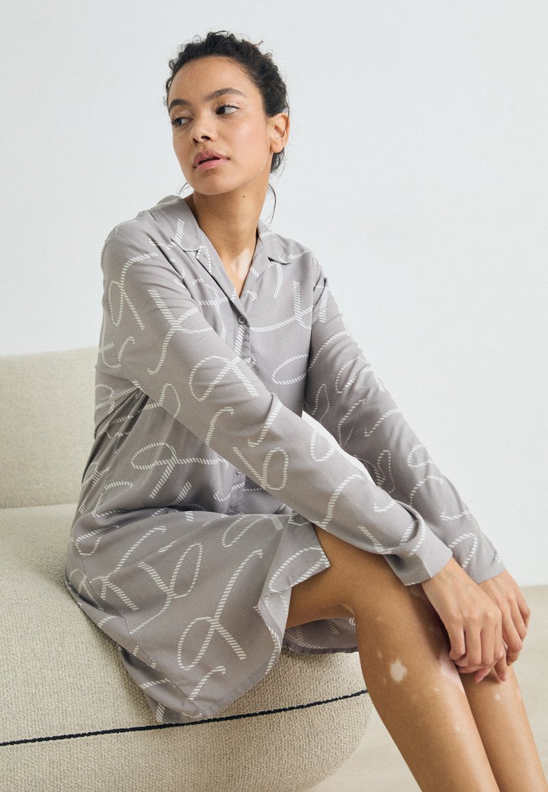 Siva obleka z dolgimi rokavi in ovratnikom, ki ima bel abstrakten vzorec. Mehak material z ohlapnim krojem, ki sega nad kolena.