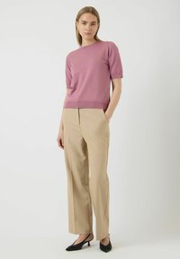 Ružičasti pulover s kratkim rukavima u kombinaciji s bež krojenim hlačama; teksturirani materijal; crne štikle na špic; minimalistički dizajn.