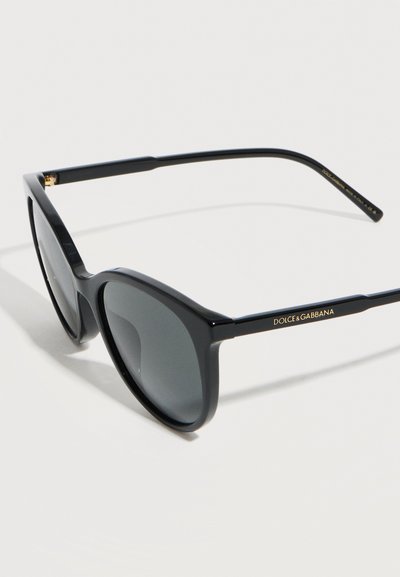 Μαύρα γυαλιά ηλίου με τετράγωνο σκελετό και σκουρόχρωμους φακούς, με το λογότυπο "Dolce & Gabbana" στο μπράτσο του σκελετού, τοποθετημένα σε λευκή επιφάνεια.