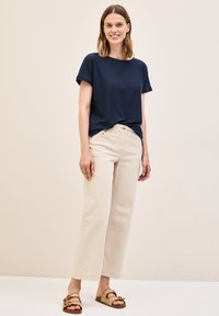 Camiseta texturizada azul marino con mangas enrolladas, pantalones de pierna ancha en beige y sandalias tejidas neutras con hebillas, exhibidas sobre un fondo claro.