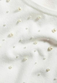 Vit tröja med en mjuk textur och utspridda pärlprydnader i olika storlekar över ytan.