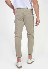 Lichtbeige slim-fit chino's met een gladde textuur, vijf zakken en subtiele ton-sur-ton stiknaden, gecombineerd met witte sneakers.