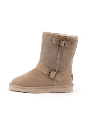 Tan suède enkellaars met een zachte faux-fur voering, verstelbare banden en een platte rubberen zool. Rond toelopend en gestikt detail aan de zijkant.