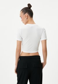 Hvid cropped t-shirt i ribbet stof med korte ærmer, parret med sorte højtaljede bukser med to baglommer.