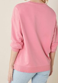 Roze pullover sweatshirt met een relaxte pasvorm, ribbelmanchetten en een zoom. De stof lijkt zacht met een gladde textuur, gecombineerd met lichtblauwe jeans.