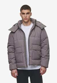 Chaqueta acolchada gris con un cuello alto, que cuenta con dos bolsillos frontales y un cierre de cremallera, fabricada con un material suave y texturizado.