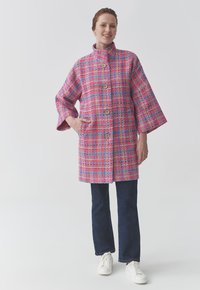 Manteau en tweed multicolore rose, bleu et violet avec un col haut, doté de boutons en bois et de manches larges. Poches des deux côtés.