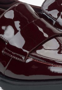 Bordeaux gepolijste leren instappers met een opvallende strikdetail, strak ontwerp en soepele textuur; zwarte zool die contrasteert met het bovenwerk.