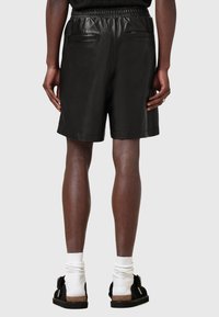 Schwarze Leder-Shorts mit elastischem Bund, ausgestattet mit zwei Gesäßtaschen und einer glatten, glänzenden Textur.