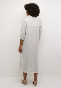 Robe midi rayée en tissu léger, présentant une légère évasement, des manches trois-quarts et des fentes latérales. Couleurs claires avec des motifs verticaux subtils.