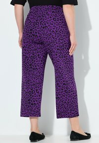 Paarse luipaardprint cropped pants met een elastische tailleband, voorzien van zwarte vlekken en een relaxed fit, gecombineerd met zwarte flats.