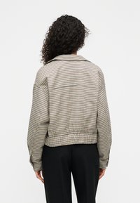 Καρό κοντό μπουφάν με γιακά, μακριά μανίκια, ελαστική μέση και μια ήπια χρωματική παλέτα σε μπεζ, μαύρο και ναυτικό μπλε.