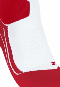 Calzini sportivi rossi e bianchi con texture a maglia fitta, blocchi di colore distintivi e un piccolo logo vicino al polsino.