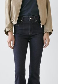 Mörkblå högmidjade jeans av denim med dragkedjefly, knappstängning och klassisk design med fem fickor. Slät textur.