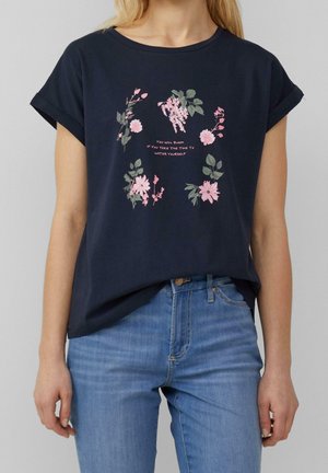 Osoba nosząca granatowy t-shirt z różowymi kwiatowymi wzorami i tekstem "You will bloom if you take the time to water yourself."